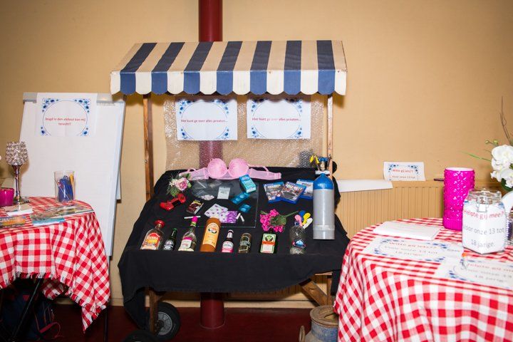 Een uitstal met diverse artikelen te koop onder een blauw-wit gestreepte luifel. Aan weerszijden liggen rood-wit geblokte tafelkleden.