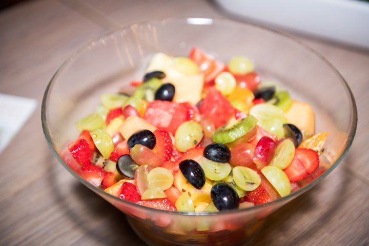 Fruitsalade in een doorzichtige glazen kom, met druiven, aardbeien, meloen en kiwi.