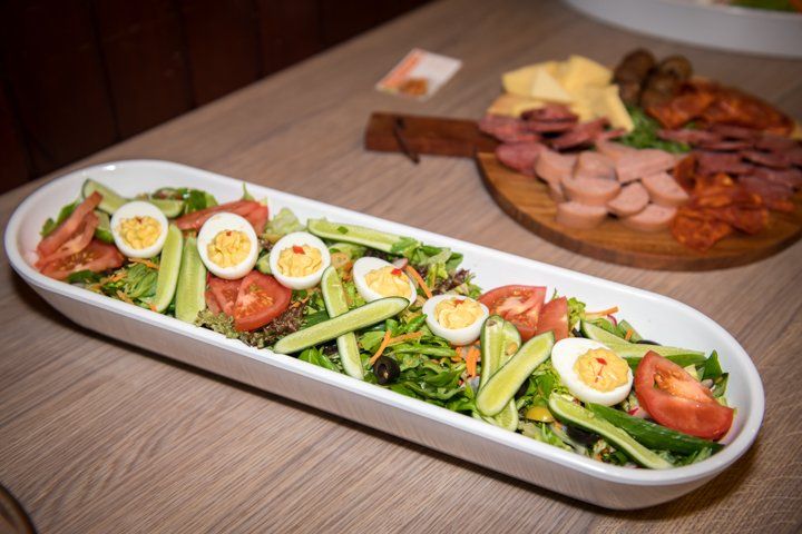Een ovale saladeschaal met hardgekookte eieren en plakjes tomaat, naast een charcuterieplank.