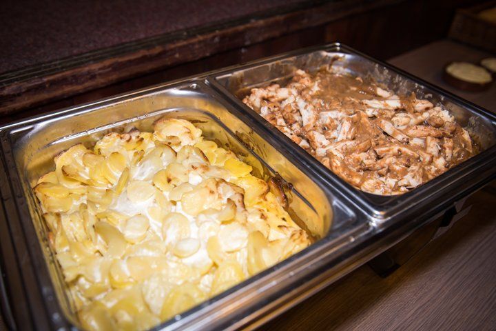 Twee warmhoudschalen: gegratineerde aardappelen en kip in jus.