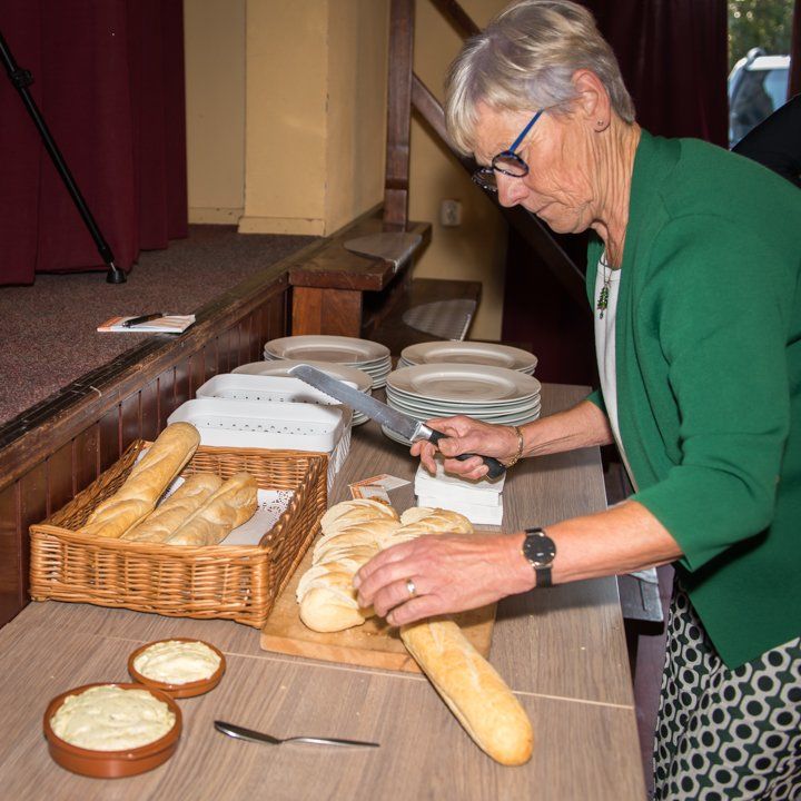 Een vrouw snijdt een stokbrood aan een tafel met borden, brood en schalen vol eten.