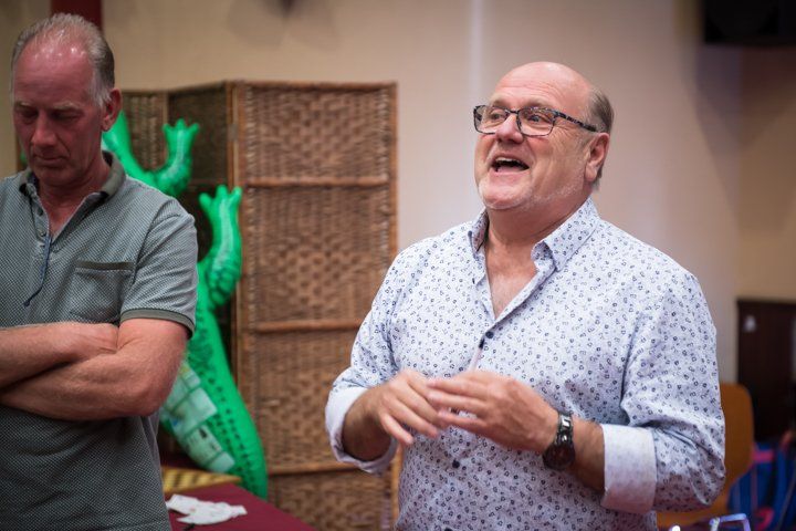 Een man met een bril spreekt en gebaart met zijn handen. Een andere man staat er vlakbij met zijn armen over elkaar.