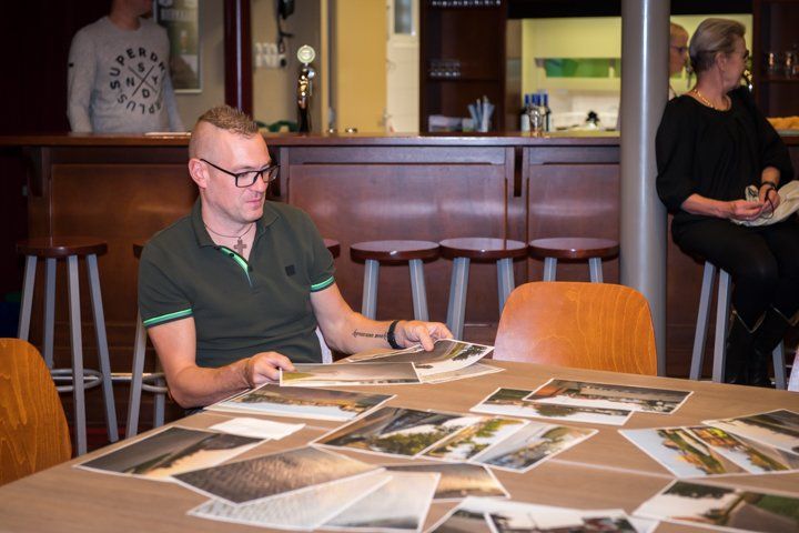 Een man aan een tafel bekijkt foto's; hij zit in een ruimte met een bar en andere mensen.