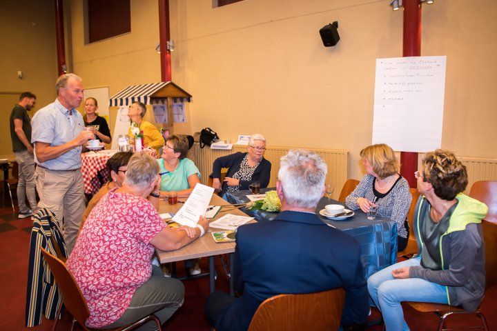 Een groep mensen zit aan een tafel en luistert naar een man die spreekt tijdens een vergadering.