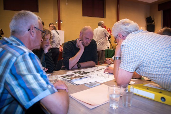 Mensen zaten rond een tafel documenten te bekijken. Een man droeg een blauw shirt, de anderen vrijetijdskleding. Binnen, geconcentreerde discussie.
