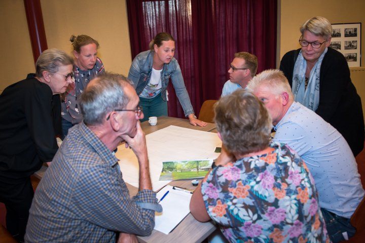 Een groep mensen zit rond een tafel en bekijkt documenten. Sommigen wijzen en bespreken ideeën in een ruimte.