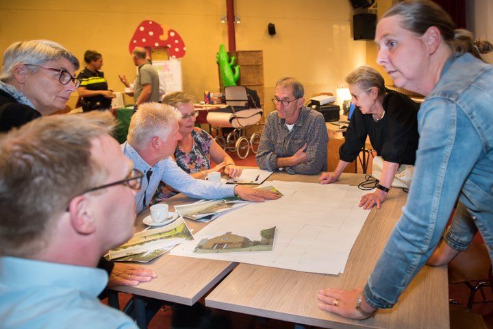 Mensen zaten rond een tafel met een wit laken, discussieerden en wezen naar papieren en modellen. Interieur.