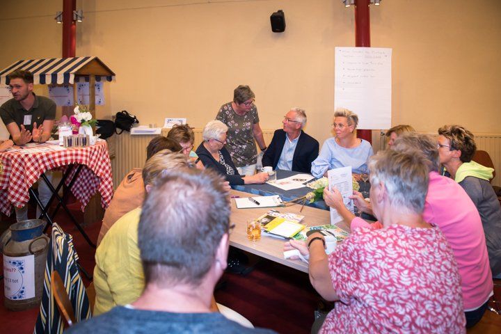 Mensen zaten rond een tafel en bespraken documenten. Op de achtergrond stond een kleine kiosk met versnaperingen.