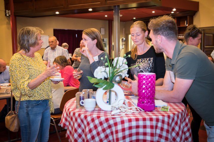 Mensen zaten rond een tafel met een rood-wit geblokt tafelkleed en voerden binnenshuis een gesprek.