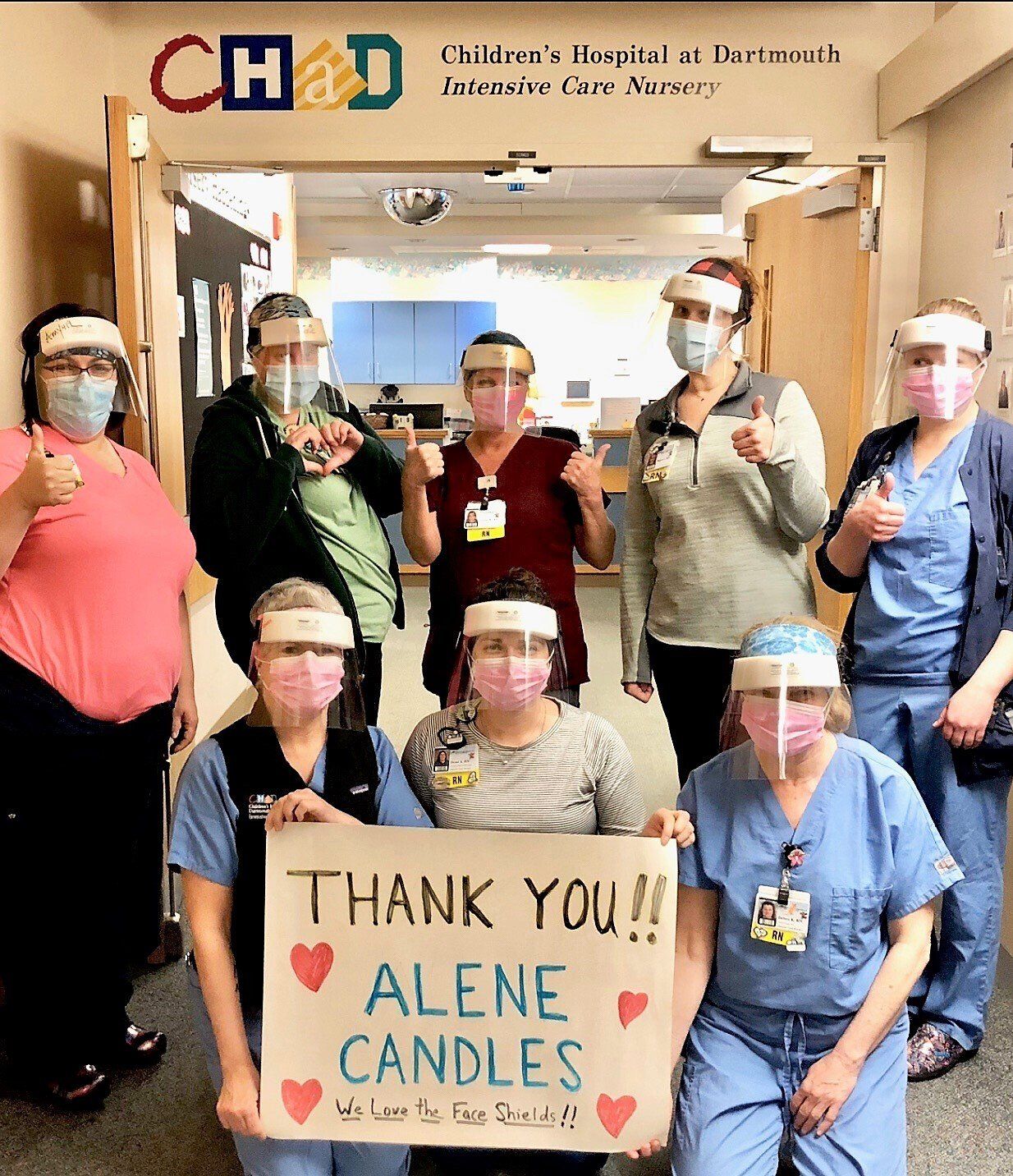 A group of nurses wearing face shields are holding a sign that says thank you alone candles
