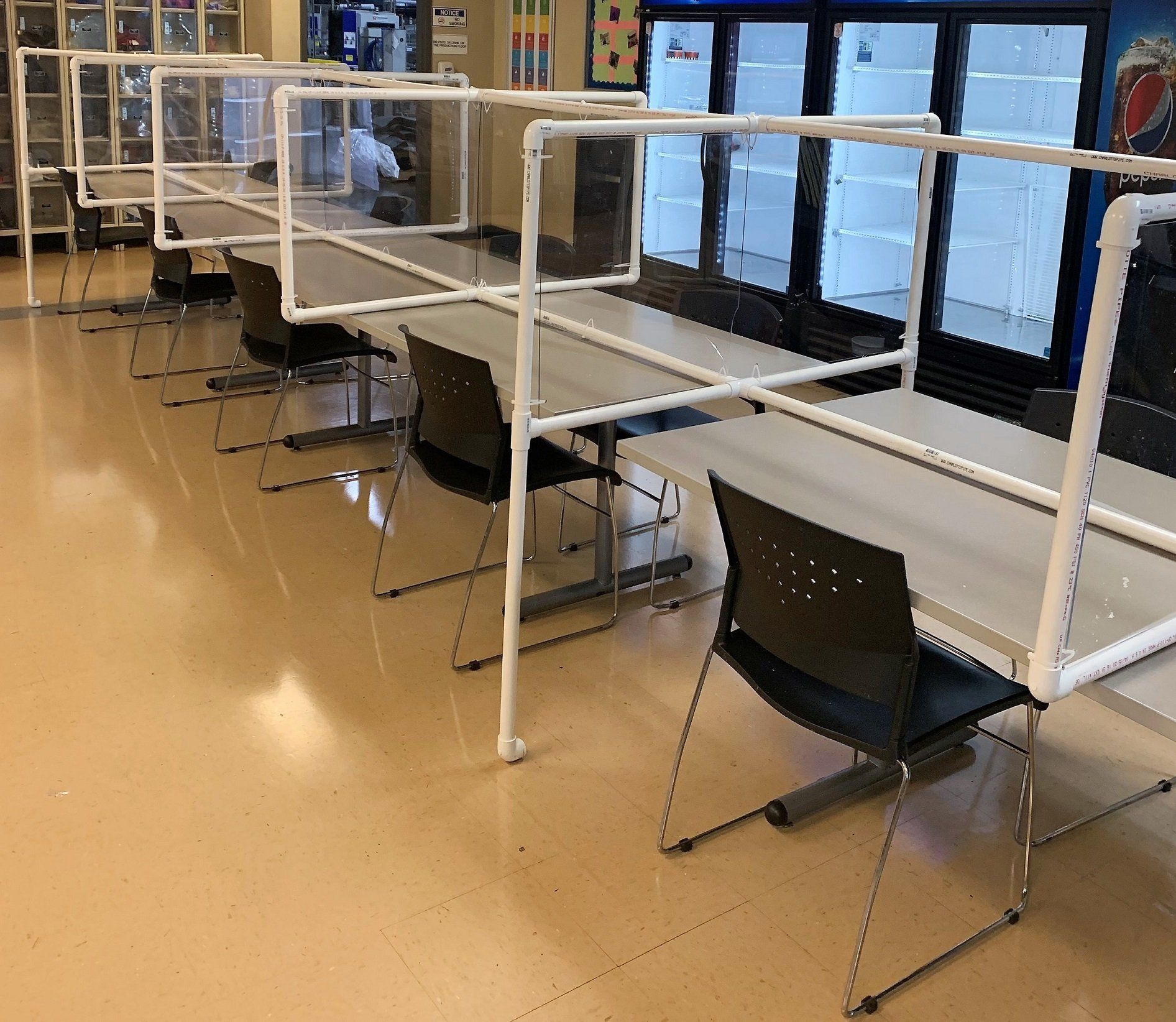 A row of tables and chairs with plastic dividers between them.
