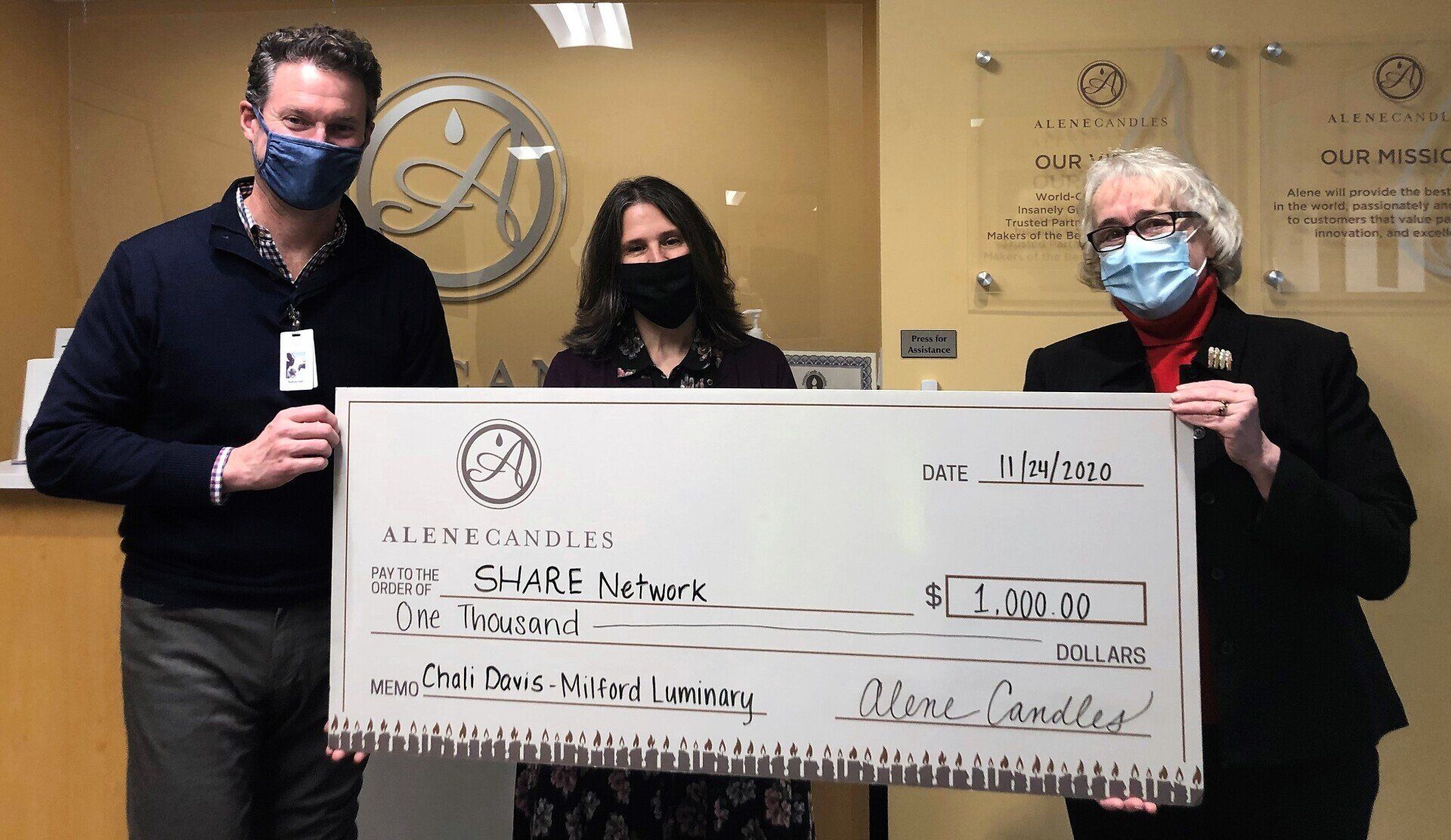 Three people wearing masks are holding a large check