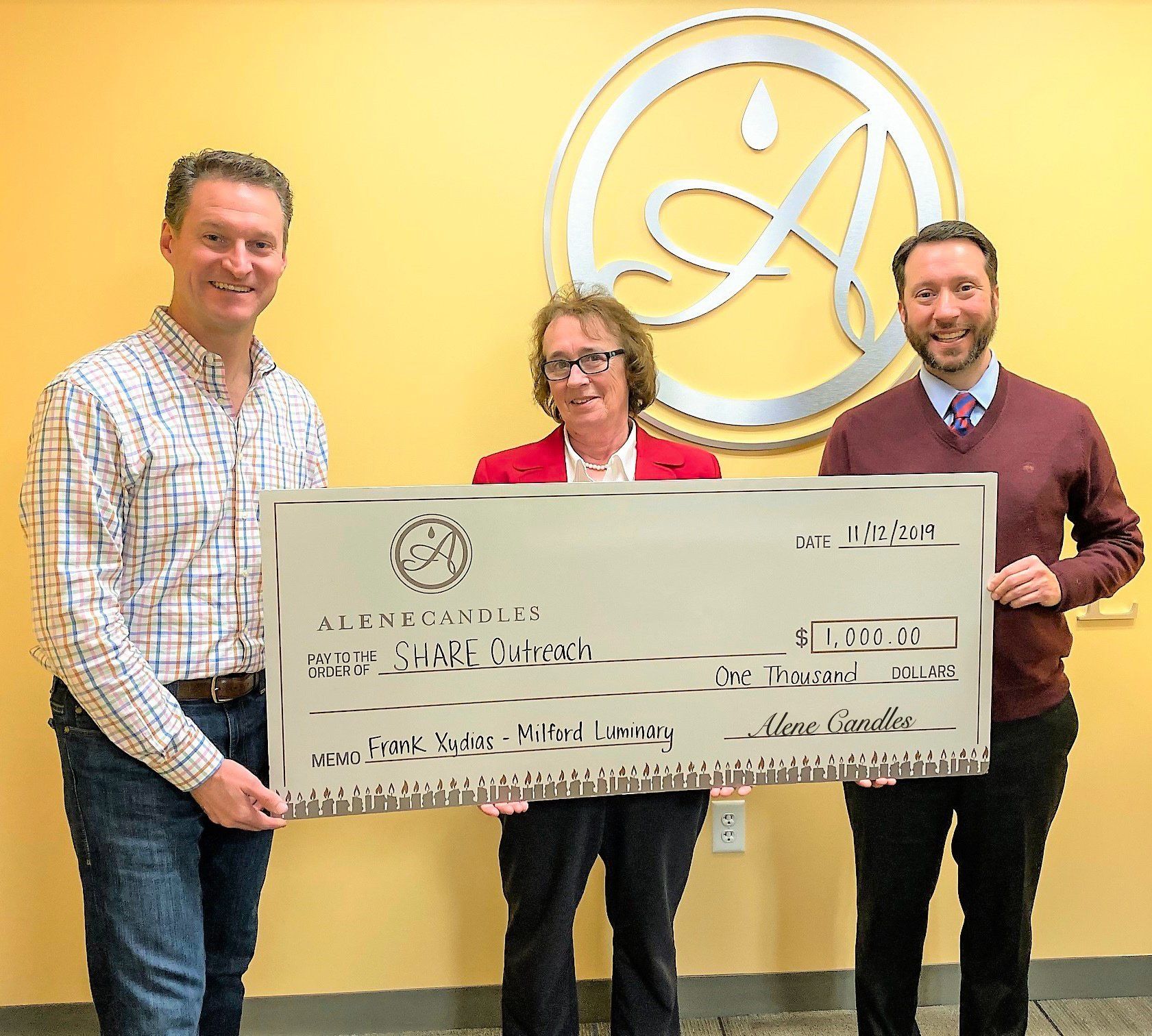 Three people holding a large check in front of a letter a