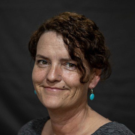 A woman with curly hair and turquoise earrings is smiling for the camera.