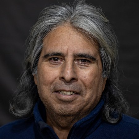 A man with long gray hair and a blue jacket is smiling for the camera.