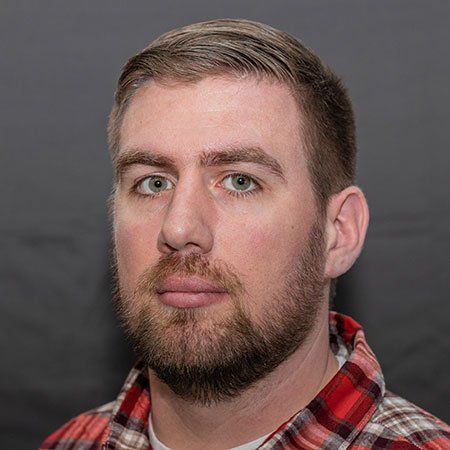 A man with a beard is wearing a plaid shirt and looking at the camera.
