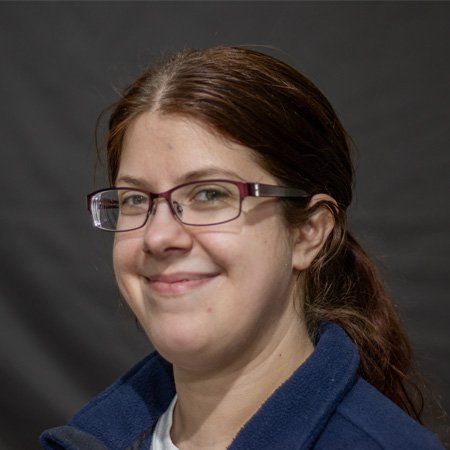 A woman wearing glasses and a blue jacket is smiling.