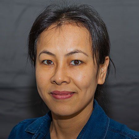 A woman in a blue denim jacket is smiling for the camera.