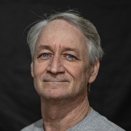 A man with gray hair and blue eyes is smiling for the camera.