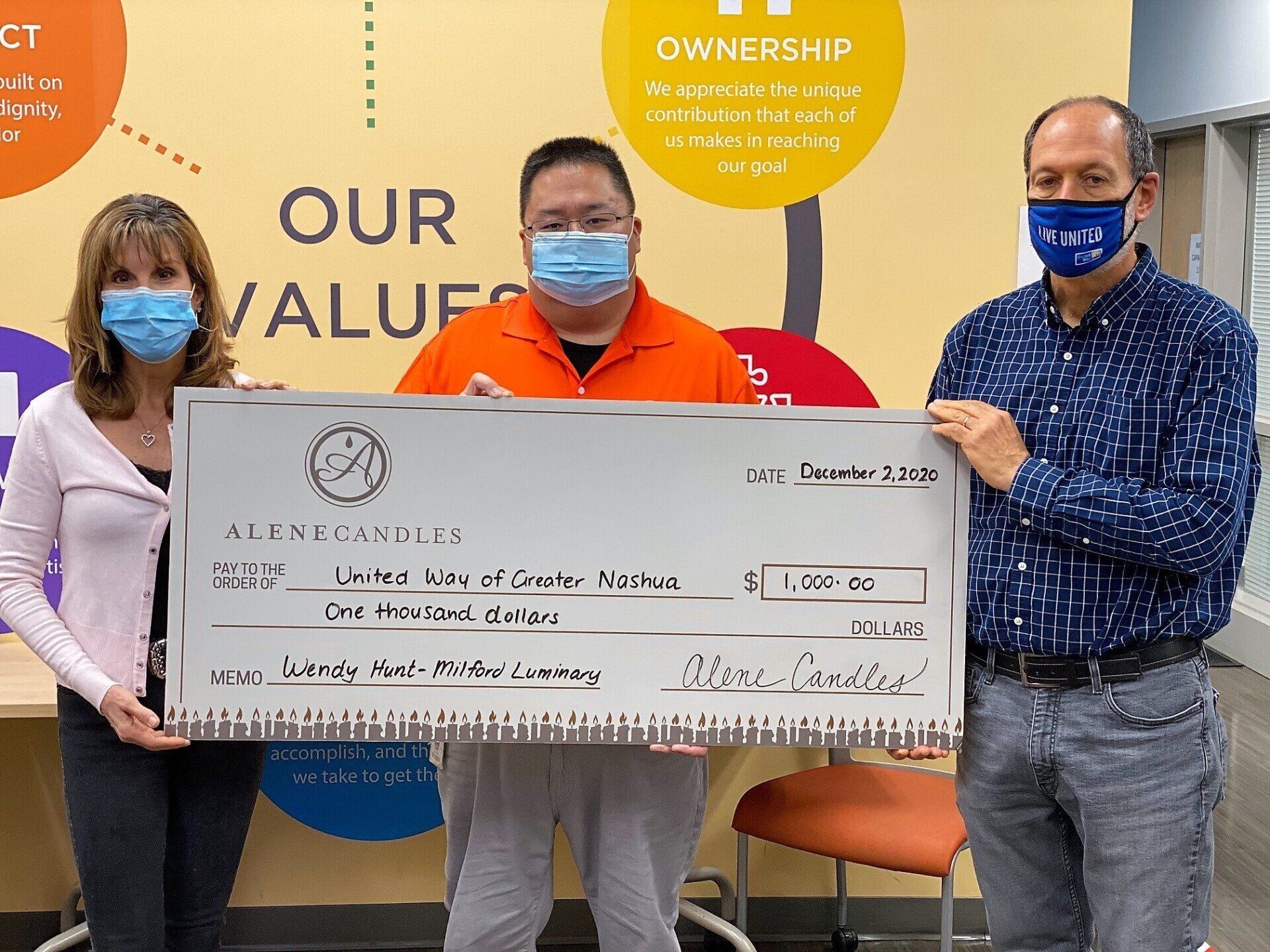 Three people wearing face masks are holding a large check