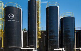 A row of black silos with yellow railings and a blue sky in the background.
