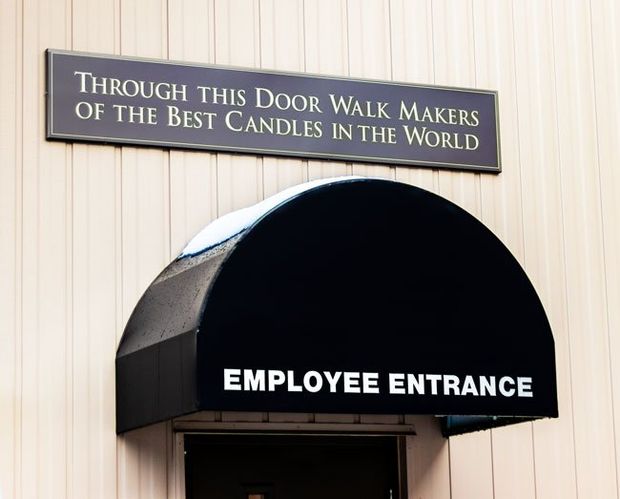 A sign on a building says through this door walk makers of the best candles in the world