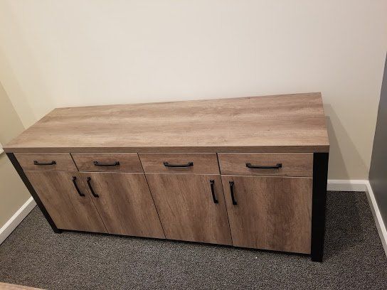 Wood-grain storage cabinet with four doors and a black top, against a beige wall on carpet.