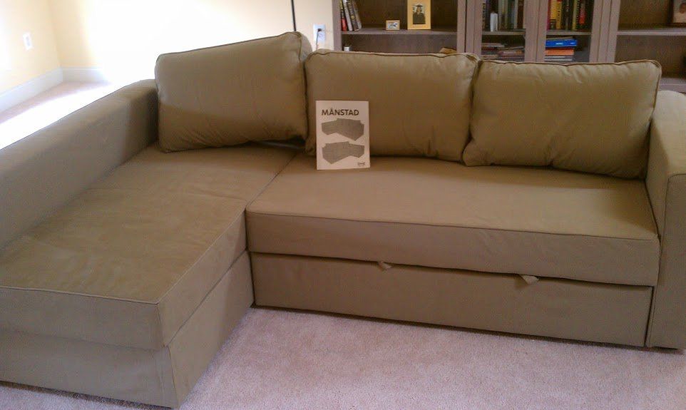Green sectional sofa with pull-out drawer, a book with images on the cushions, in a living room.