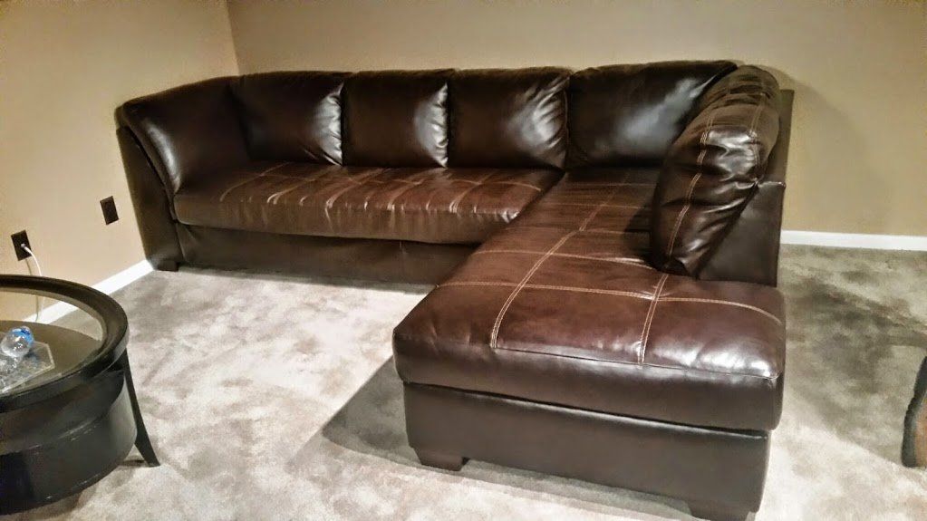 Brown leather sectional sofa with chaise lounge on gray carpet.