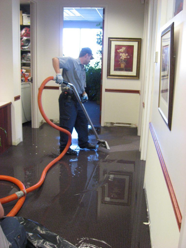 A man is using an orange hose to clean a flooded hallway