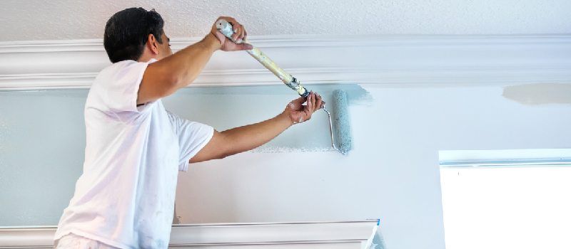 A man is painting a wall with a paint roller.