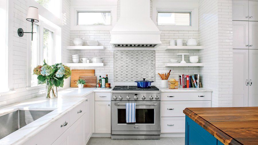 A kitchen with white cabinets , a stove , a sink , and a blue island.