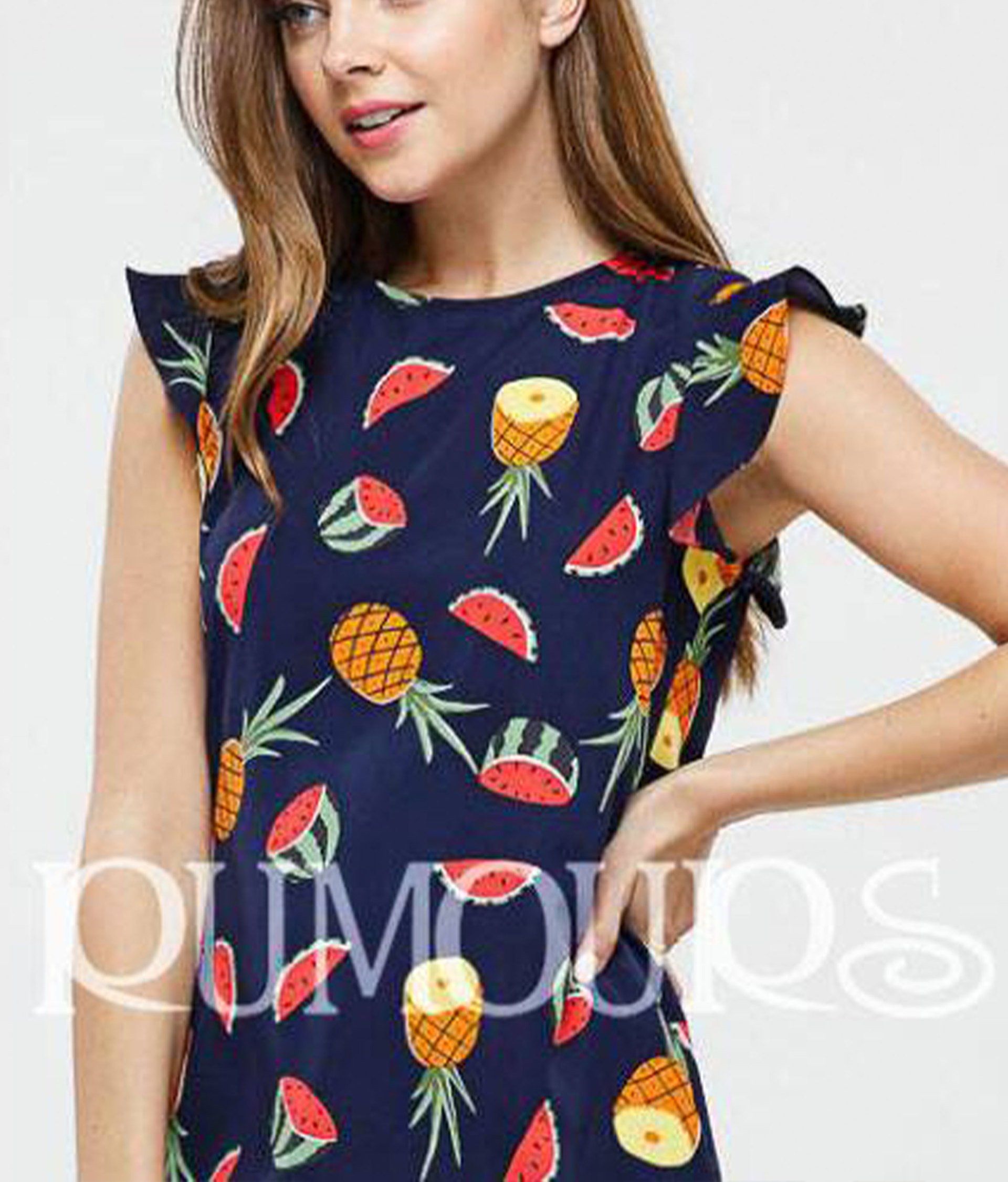 Woman wearing a navy dress with a pineapple and watermelon print; ruffles on the shoulders.