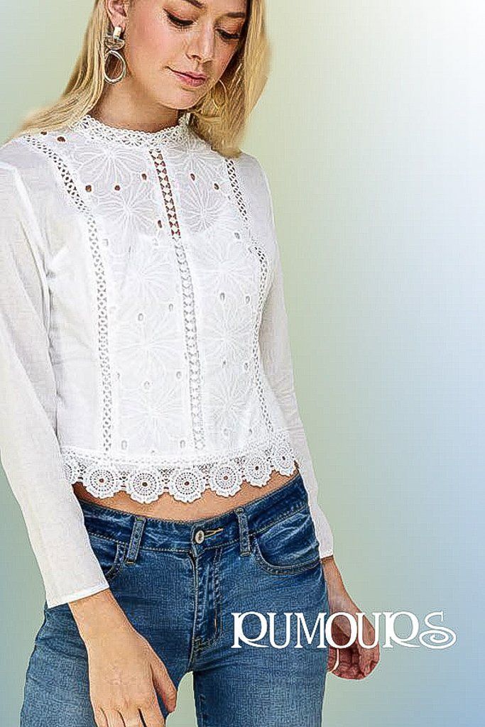 Woman wearing a white lace top, with long sleeves, and high collar, paired with acid wash jeans.