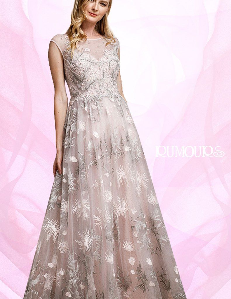 Woman in a floor-length, embellished gown with sheer overlay. She stands in front of a pink backdrop.