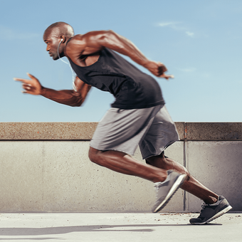 Man running on a concrete surface against a blue sky, wearing athletic clothes and earbuds.