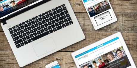 Laptop, tablet, and phone displaying a website on a wooden surface.