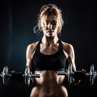 Woman in black sports bra lifts dumbbells in dark setting.