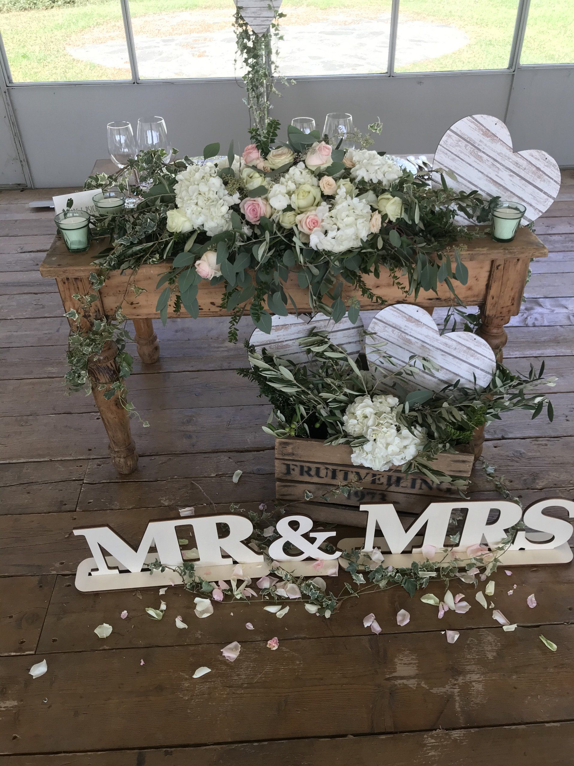 Composizione floreale per matrimonio su tavoli di legno con fiori bianchi e un cartello