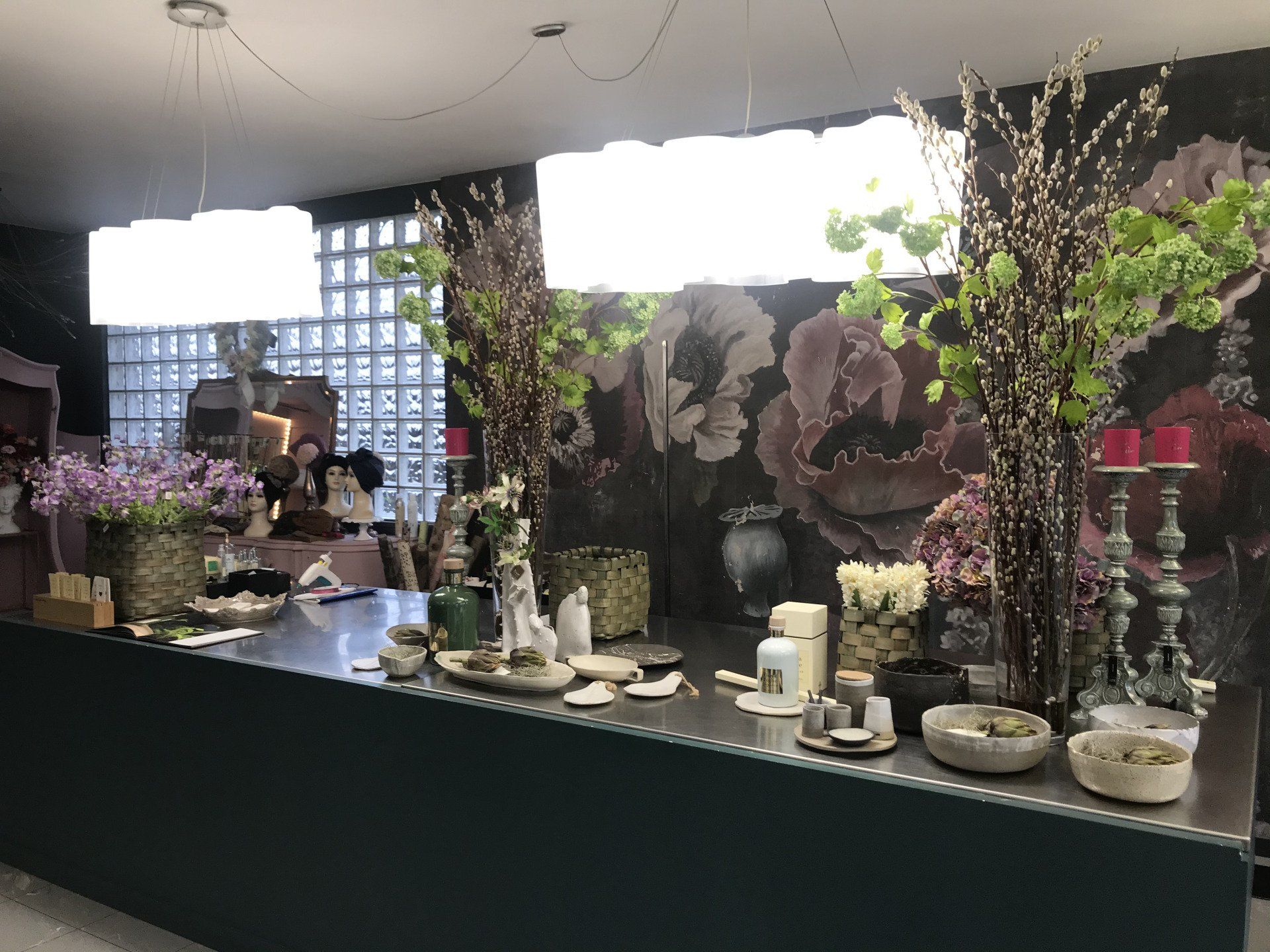 Bancone di un negozio di fiori con composizioni floreali, candele e vasi in esposizione.