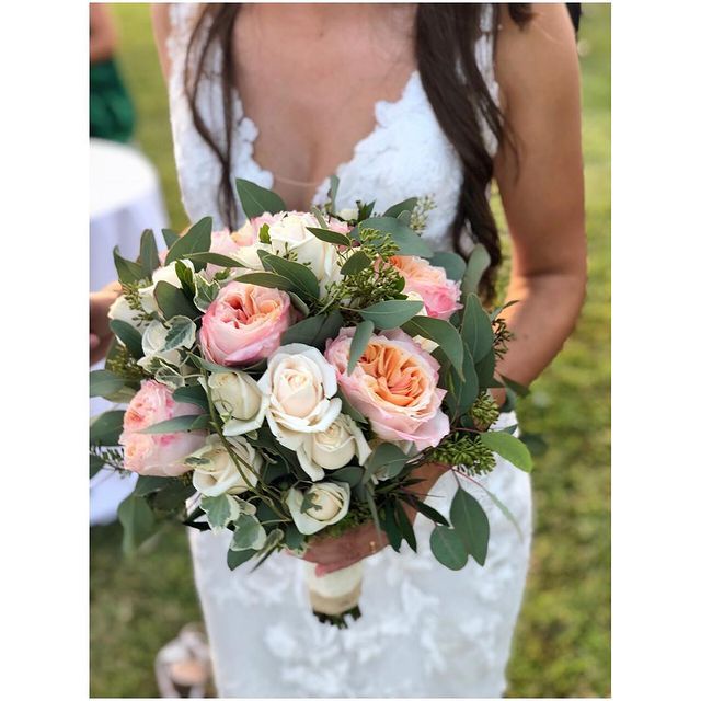 Sposa con in mano un bouquet di rose bianche e rosa con verde in un giardino.