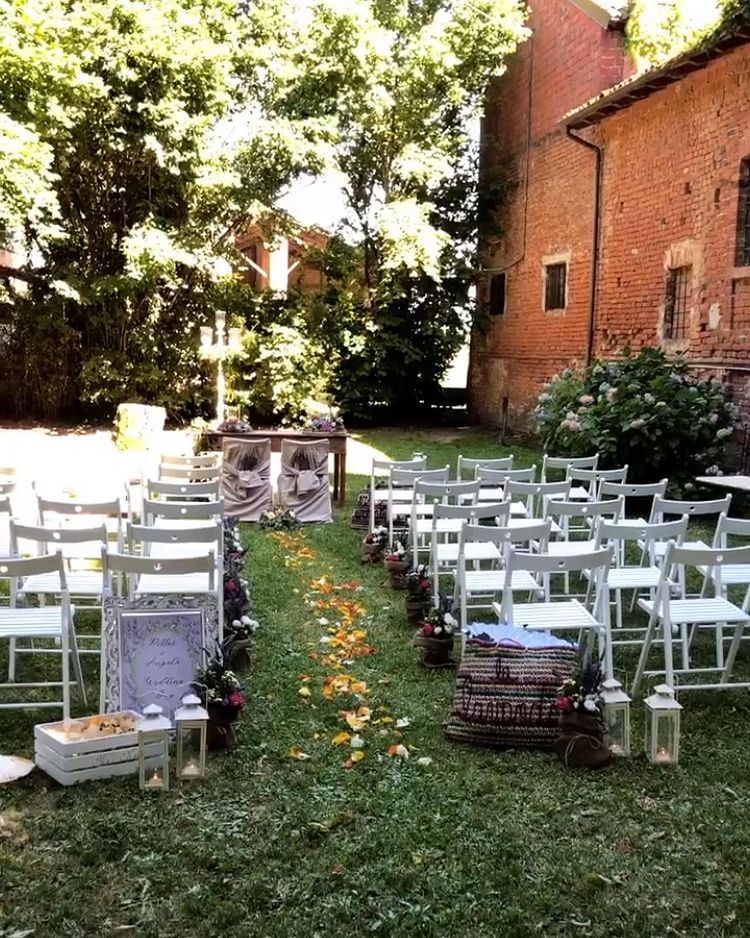 Allestimento per la cerimonia nuziale all'aperto in un cortile con giardino, con sedie bianche e un corridoio di fiori.