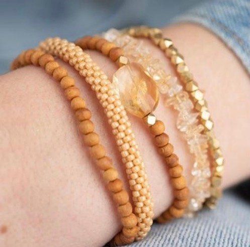 Primo piano di un polso con braccialetti di perline sovrapposti nei toni del marrone chiaro, dell'oro e del trasparente.