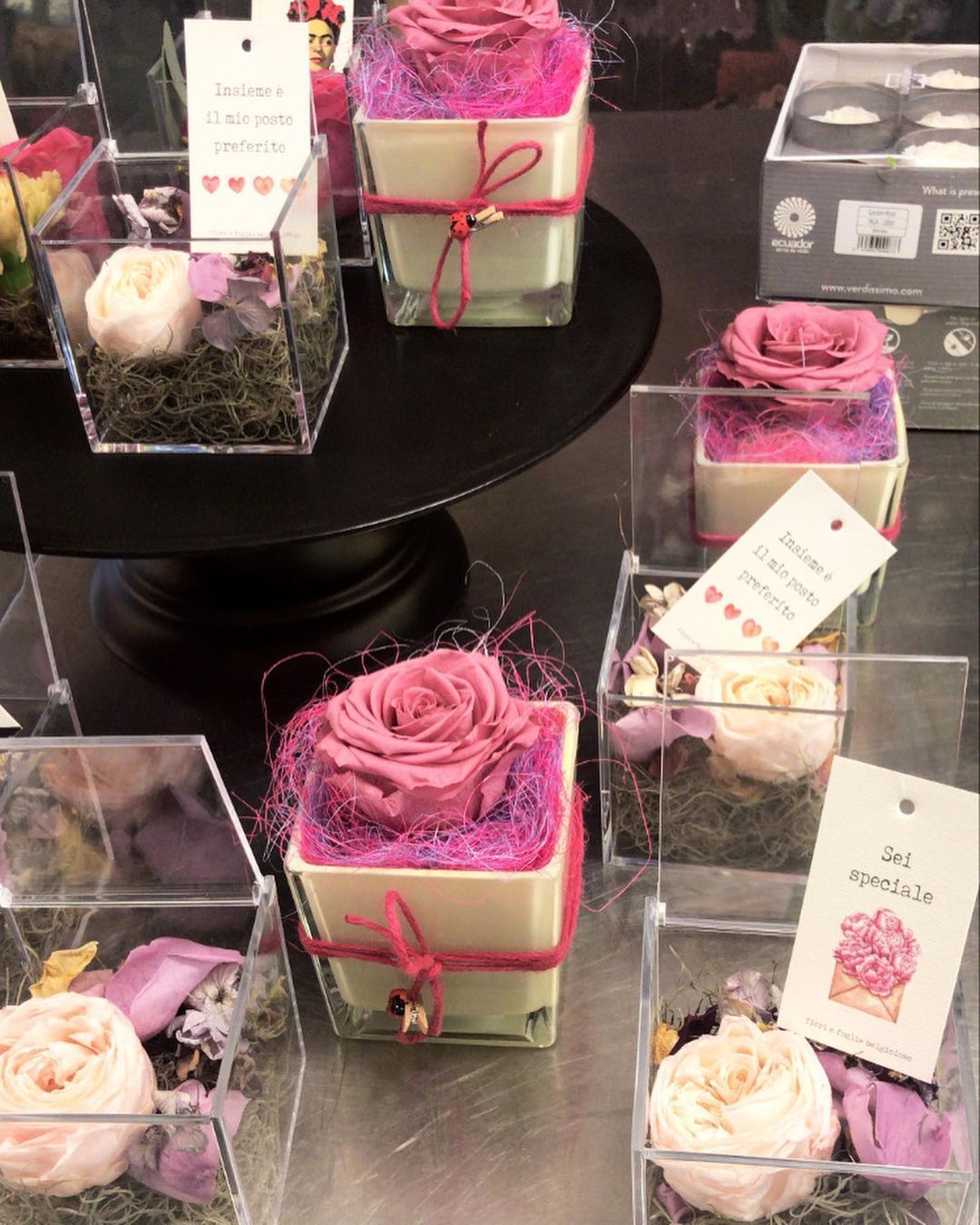 Piccola esposizione di composizioni floreali regalo rosa e bianche in scatola, su un supporto nero.