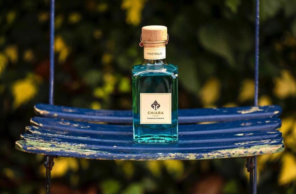 Flacone di profumo blu su una panchina blu con uno sfondo esterno sfocato verde e giallo.