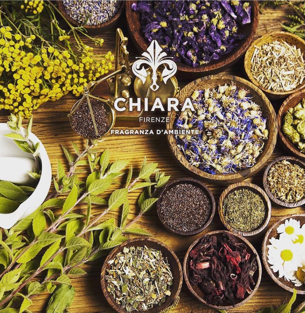 Assortimento di erbe aromatiche e fiori secchi in ciotole su una superficie rustica con il logo Chiara al centro.