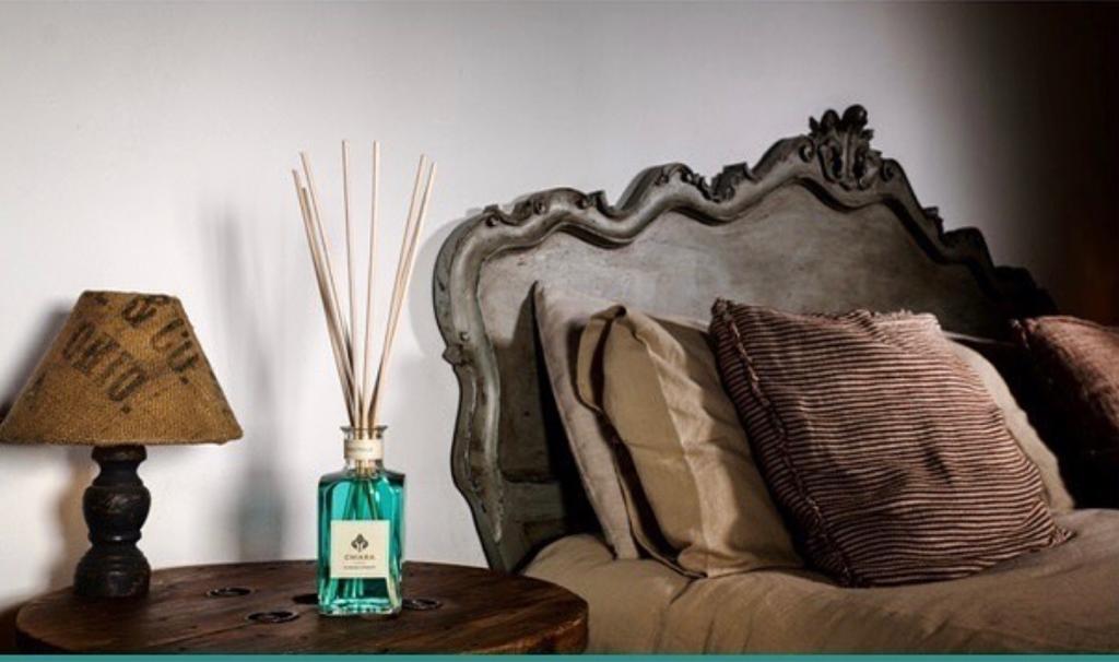 Comodino vintage da camera da letto con lampada, diffusore a bastoncini e testiera imbottita decorata con cuscini.