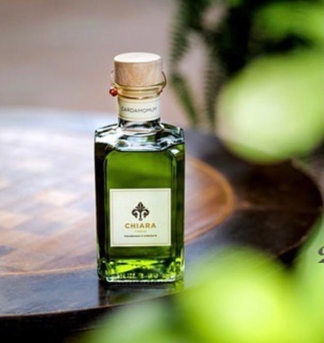 Flacone di profumo verde con tappo di sughero e scritta Chiara su un vassoio di legno, con sfondo verde sfocato.