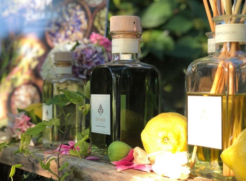 Profumo con tappi di sughero su una composizione floreale dal sole: uno verde, uno ambrato, uno sfocato sullo sfondo.