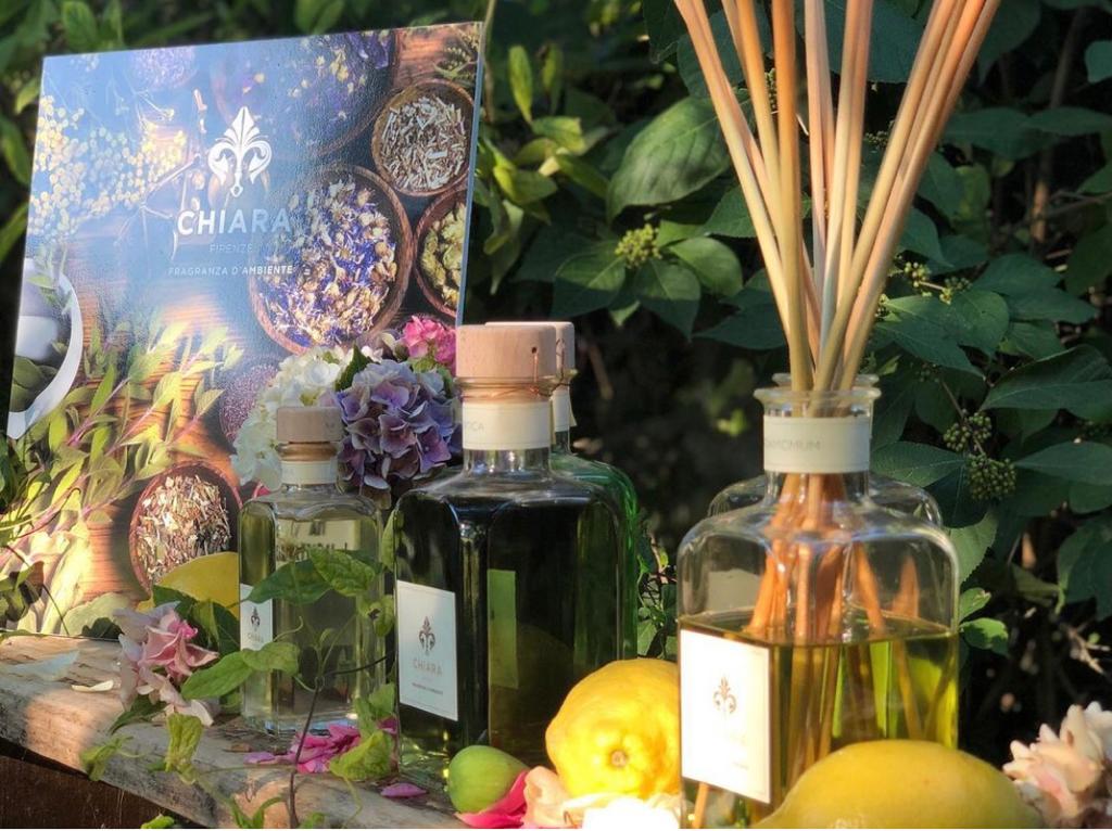 Bottiglie diffusore di fragranze con bastoncini, limoni e fiori su un tavolo decorato con foglie.